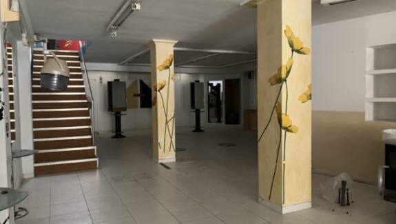 Interior del local comercial en venta en Tarragona, con columnas decoradas, escaleras y equipamiento de antigua escuela de peluquería.