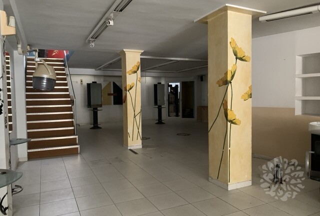 Interior del local comercial en venta en Tarragona, con columnas decoradas, escaleras y equipamiento de antigua escuela de peluquería.